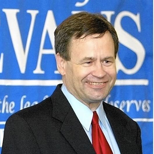Lane Evans smiling in a dark suit and red tie in front of a blue EVANS campaign banner.